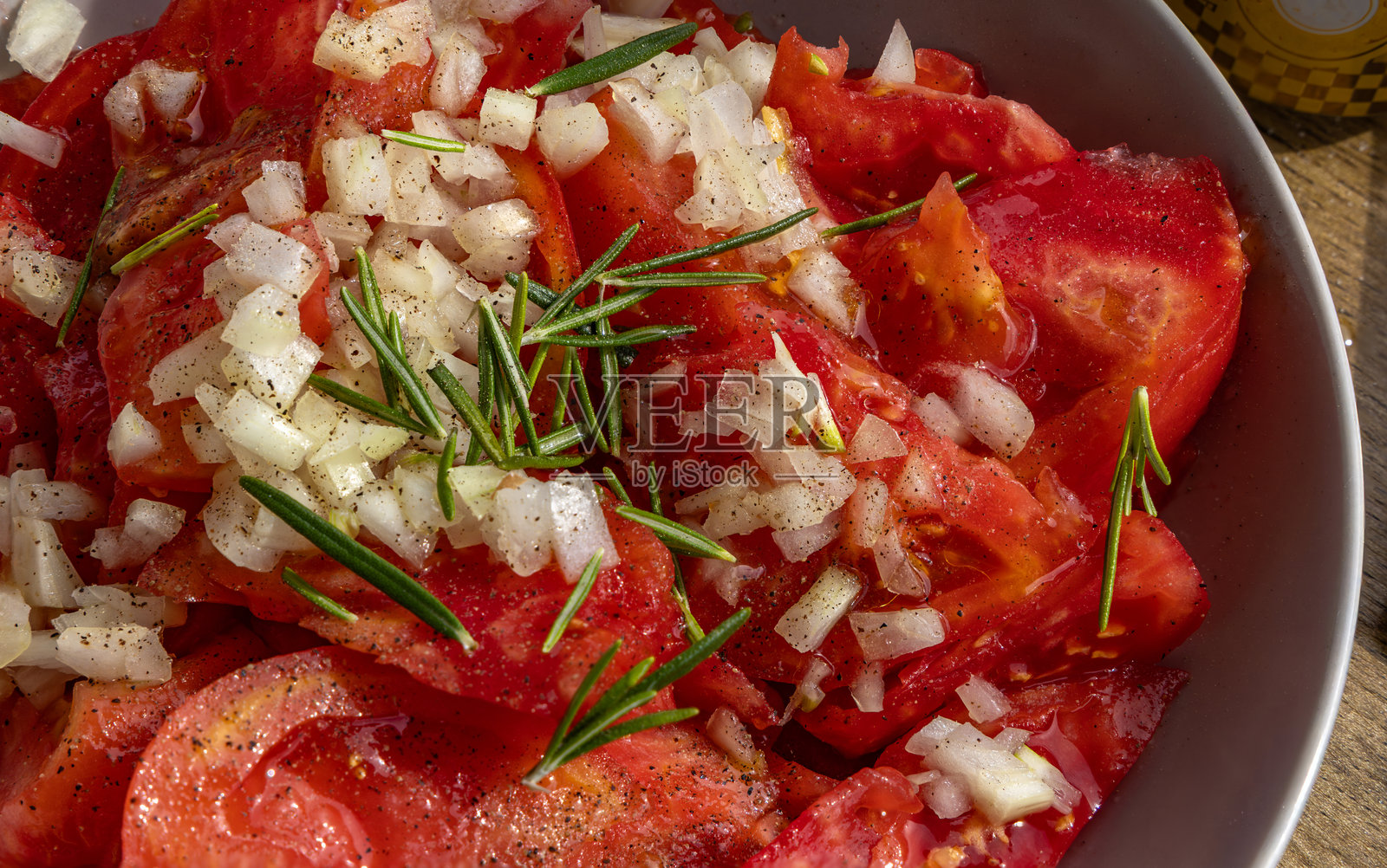 一盘切好的新鲜红番茄,淋上克罗地亚橄榄油,配有洋葱和迷迭香,背景为白色。照片摄影图片