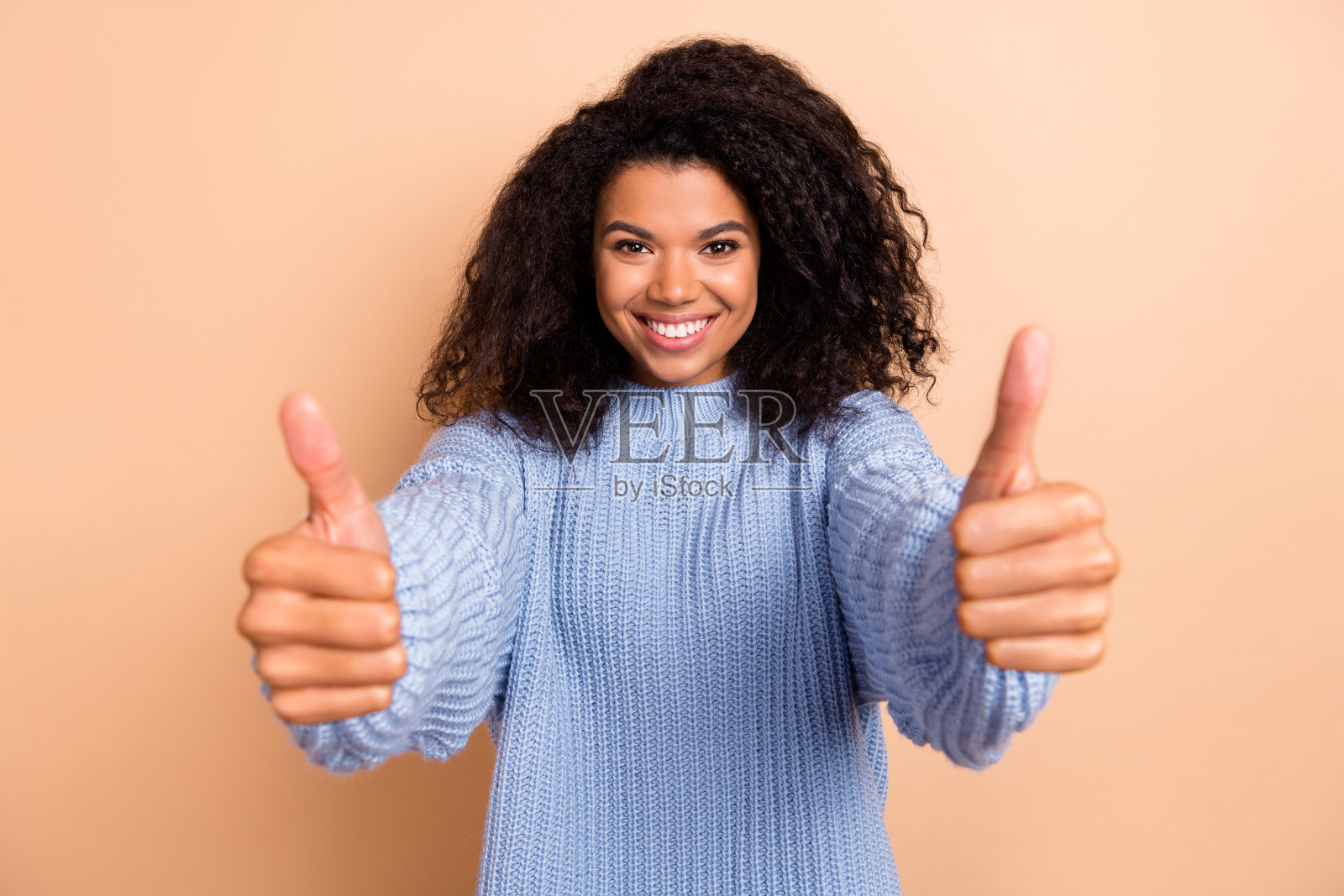 年轻快乐的女孩竖起大拇指,适合广告宣传,背景为米色。照片摄影图片