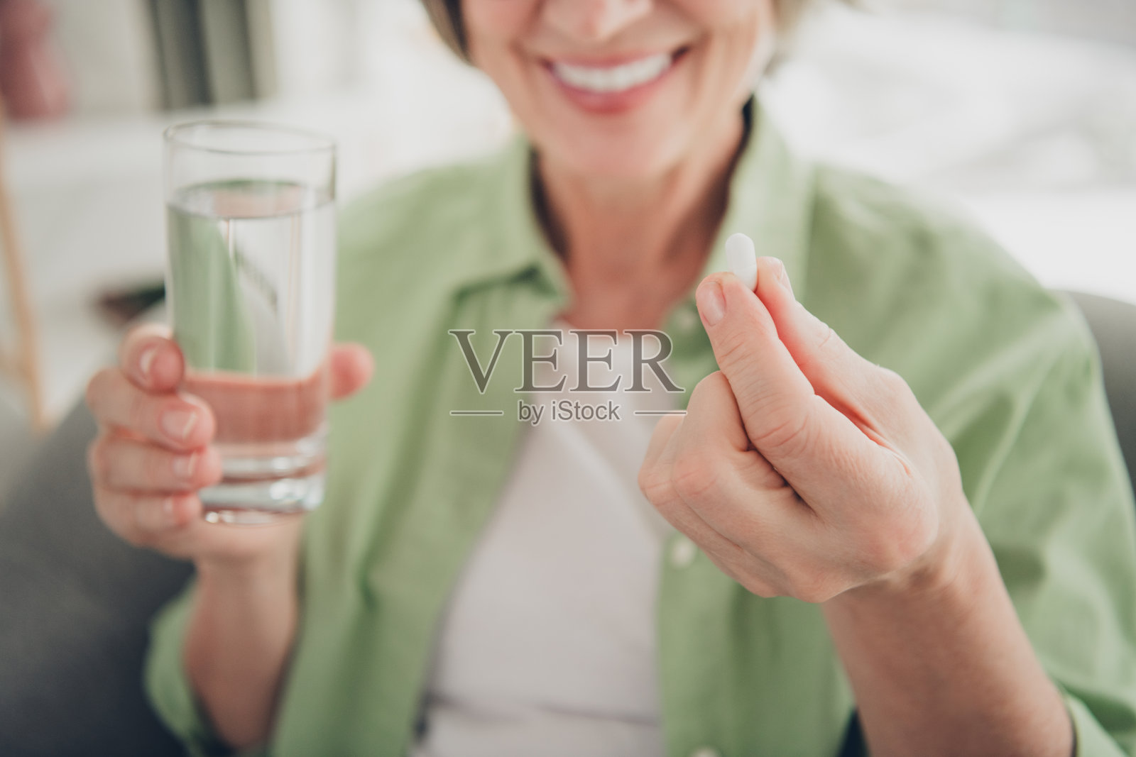 微笑的老年女性在家中轻松的环境中,手握药丸和一杯水。照片摄影图片