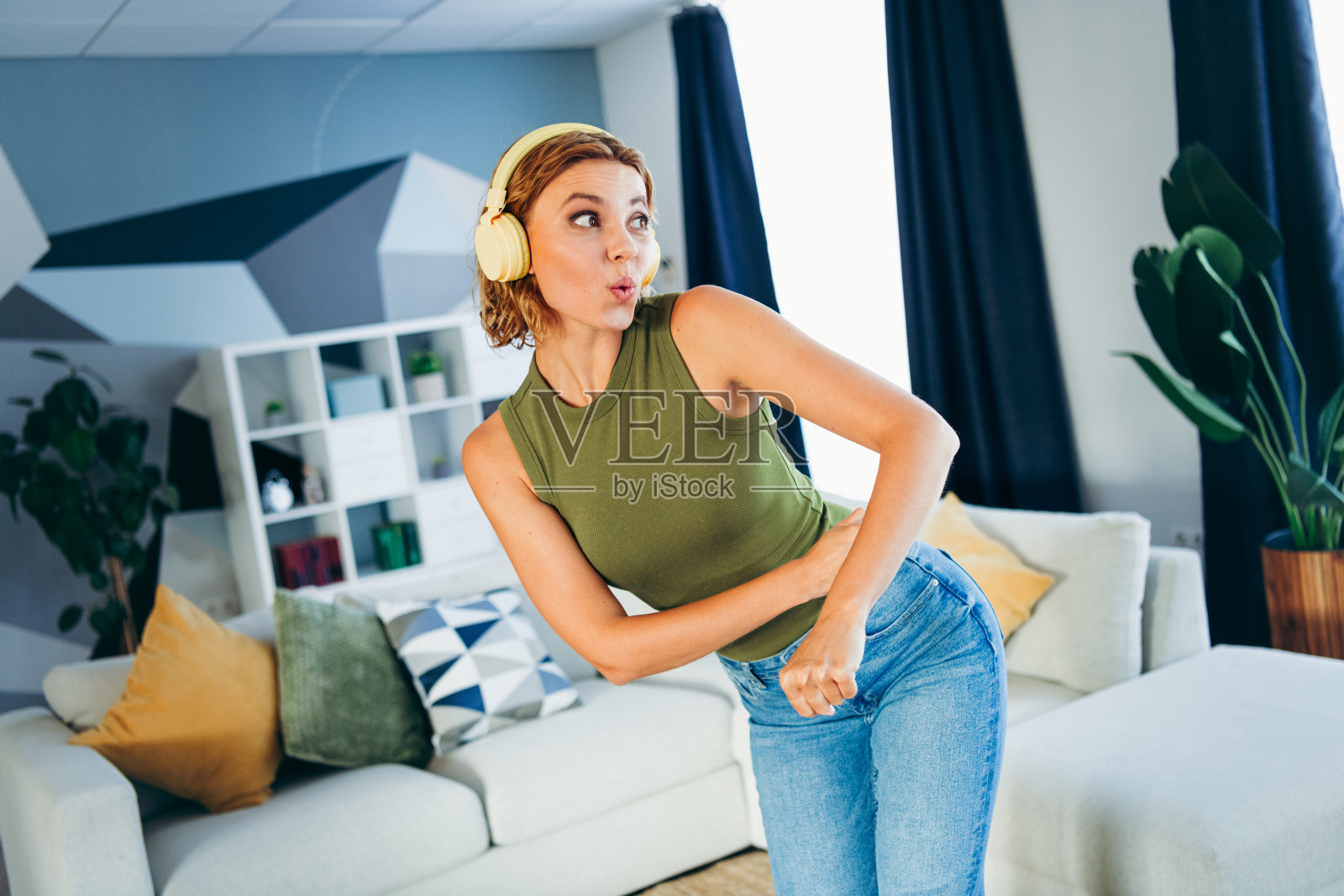 可爱的女性穿着休闲服,在舒适的客厅环境中享受音乐,佩戴着耳机,度过闲暇时光。照片摄影图片