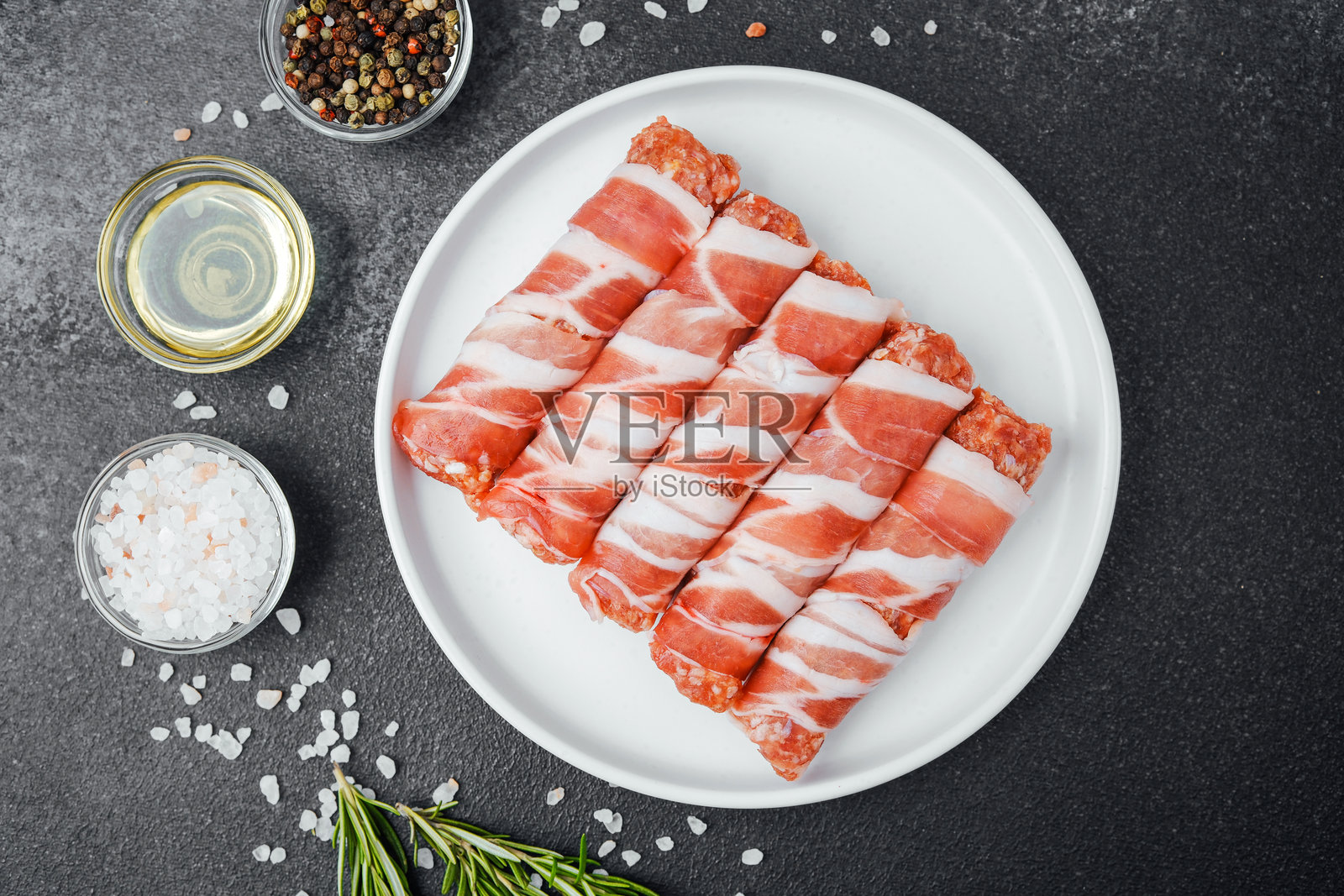 生培根裹肉卷放在白色盘子上,旁边有香草和香料照片摄影图片