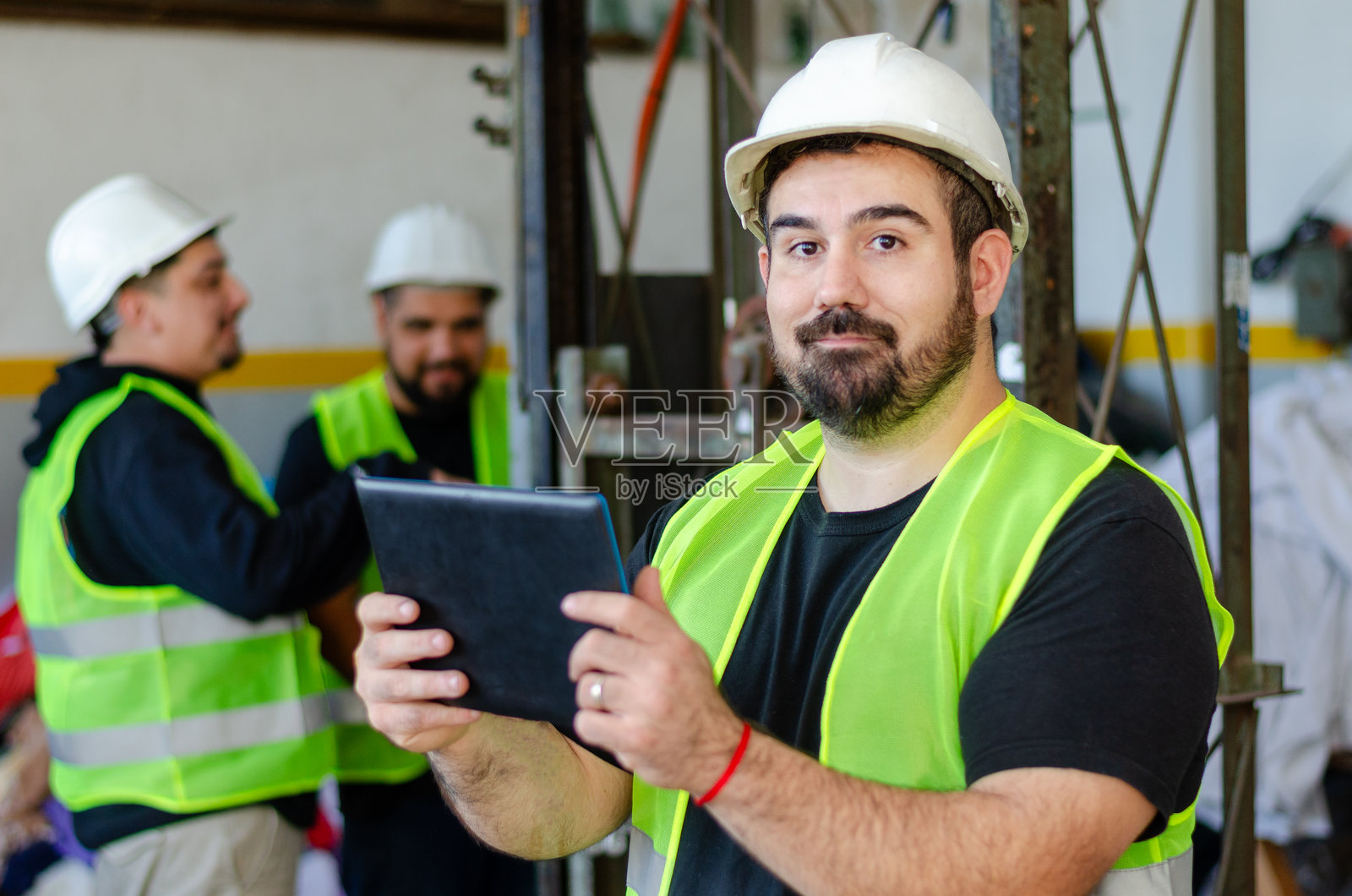 男性工厂或工业工人穿着安全装备,使用数字平板电脑。回收工厂概念。背景中有工人。照片摄影图片