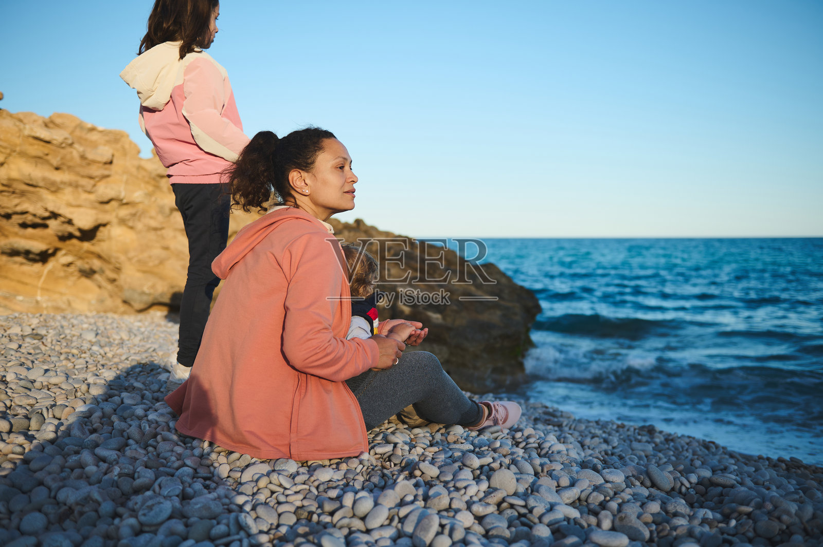 两位女性在宁静的环境中,坐在岩石海滩上放松,面朝大海。照片摄影图片