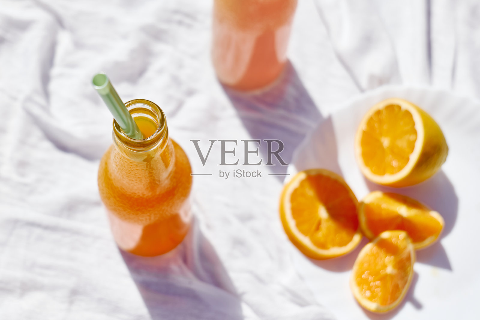 清凉的夏季饮品。桌上摆放着装有饮用吸管的新鲜橙汁瓶,桌布为白色。照片摄影图片