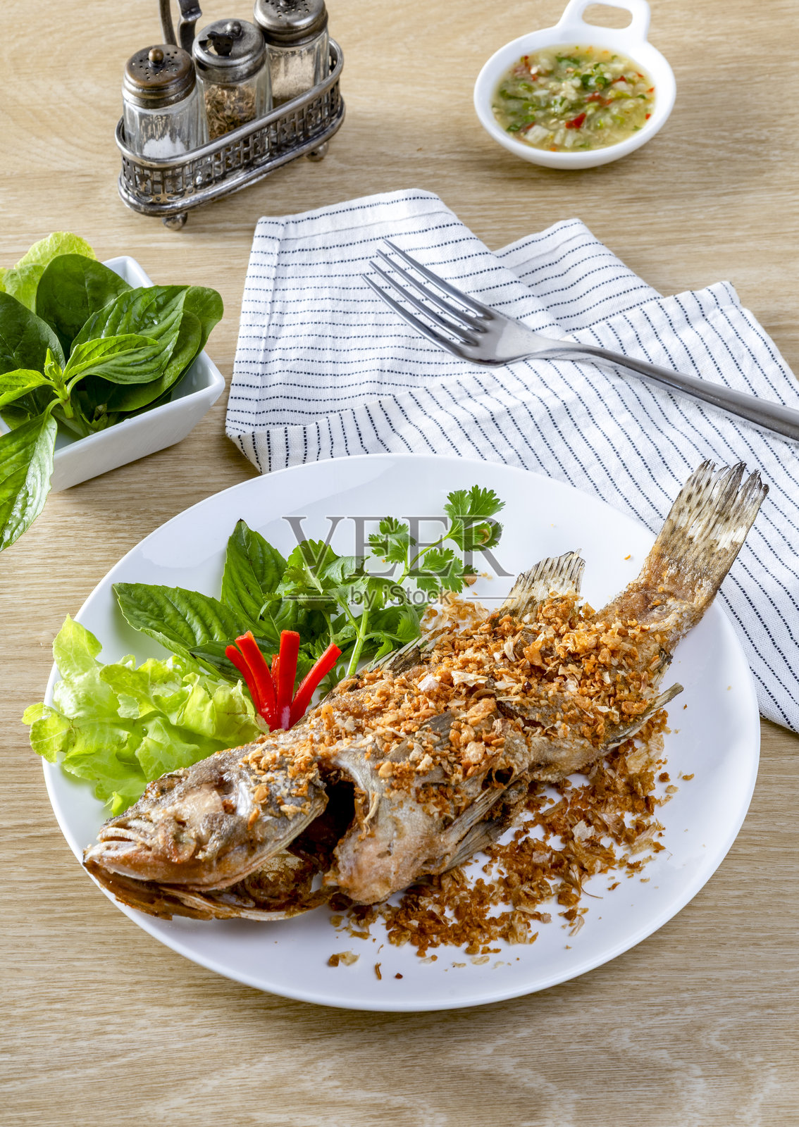 炸海鲈鱼撒上中国大蒜,炸至金黄酥脆,放在白色盘子里,摆放在桌子上。照片摄影图片