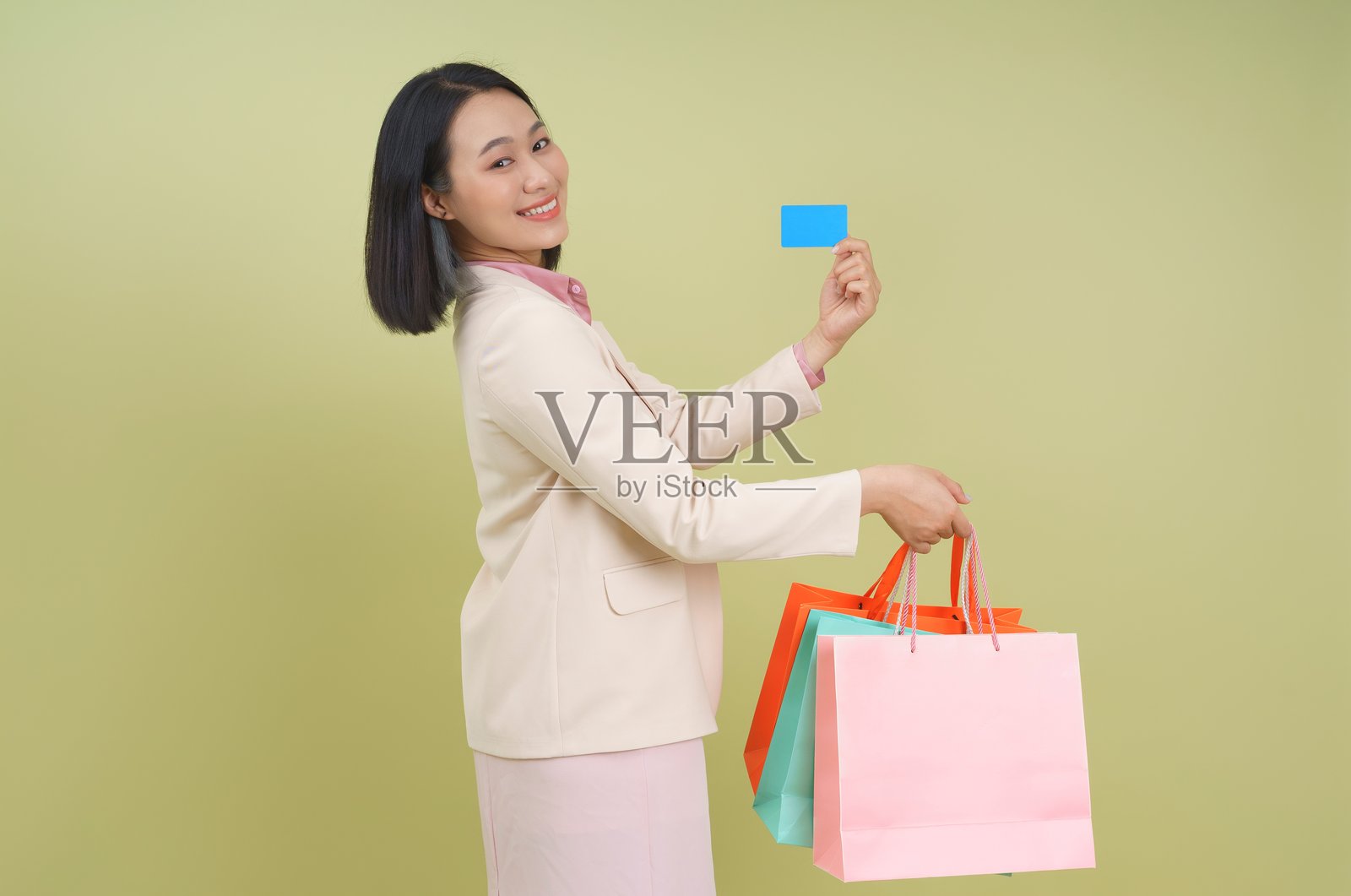 女人在绿色背景下手持购物袋和信用卡,享受轻松的购物时刻照片摄影图片