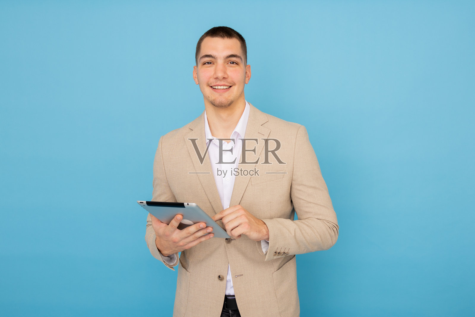 微笑的职业商人在蓝色背景的工作室中使用数字平板电脑。照片摄影图片