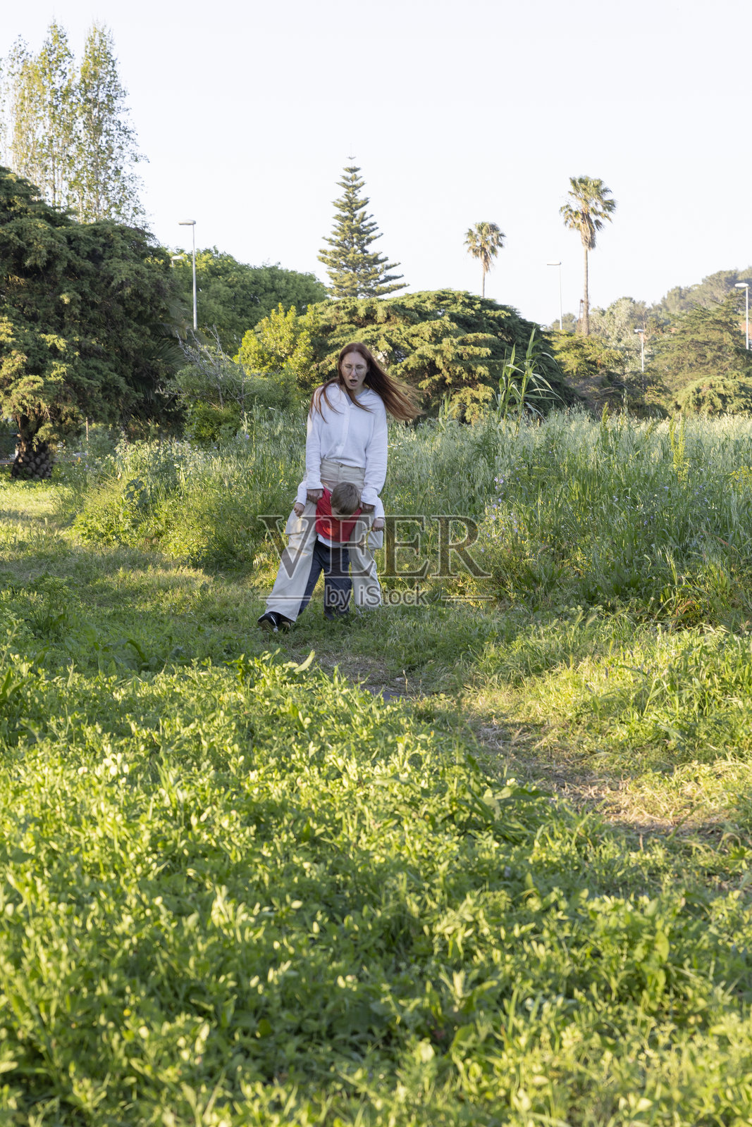 母亲在春天的公园草地上抱着儿子散步照片摄影图片