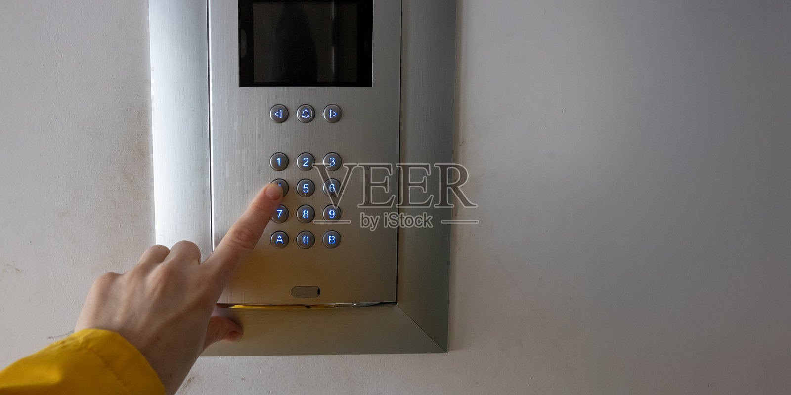 一个人手在公寓大楼入口的键盘上按下按钮。该访问控制系统用于通过个人密码进行安全进入。照片摄影图片