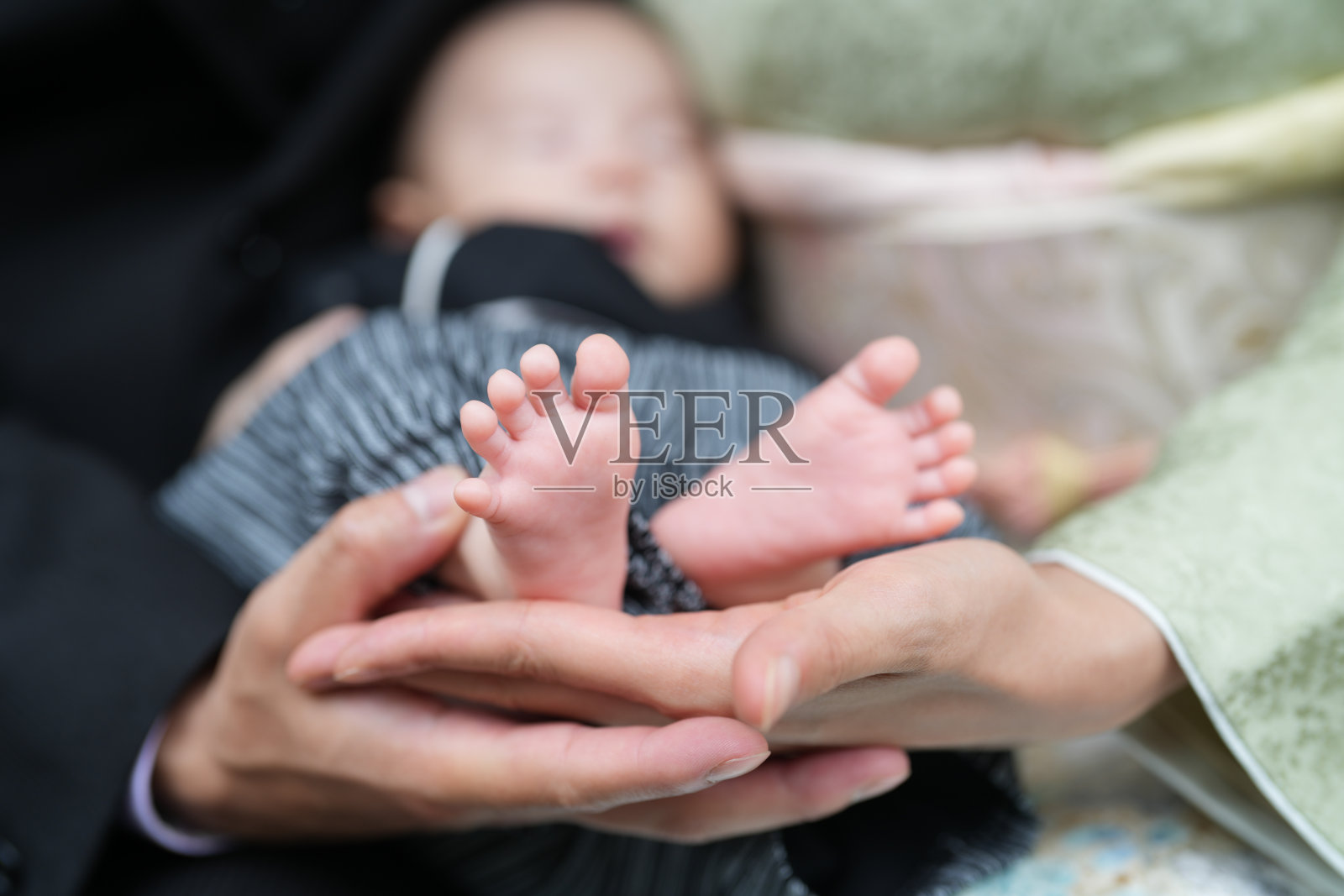 在日本的一座寺庙里,五月的春天,一名穿着袴的一个月大的日本婴儿被一位穿着和服的母亲和一位身穿西装的二十多岁男子抱着,他们的手支撑着,脚朝前。照片摄影图片