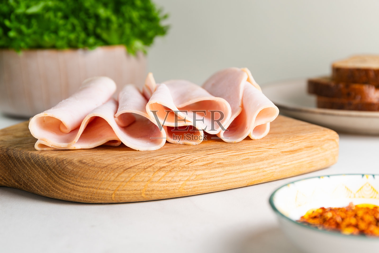 切好的火鸡火腿优雅地折叠在木砧板上,背景是新鲜的三明治配料。照片摄影图片
