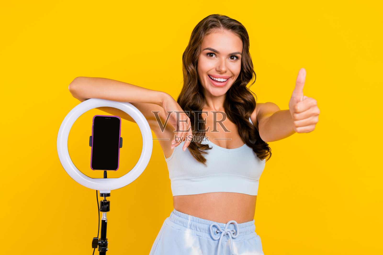 穿着运动服的可靠女性竖起大拇指,给予积极的博客反馈,背景为黄色。照片摄影图片