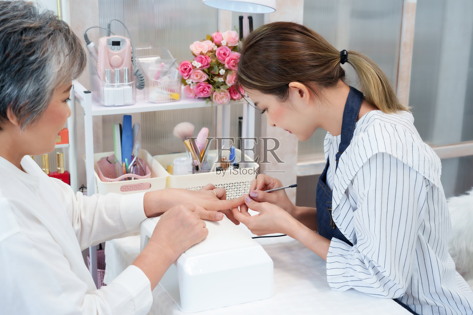 美甲师在舒适的小型商业环境中,仔细为一位年长的亚洲女性修剪指甲,宣传个人护理、美容卫生、健康放松的生活方式。照片摄影图片