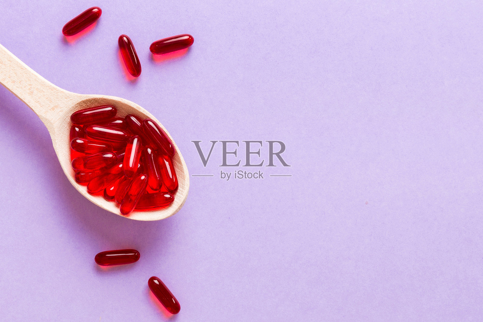 彩色背景上的勺子里装着维生素胶囊。药丸作为健康餐食。红色软胶维生素补充剂胶囊放在勺子上。照片摄影图片