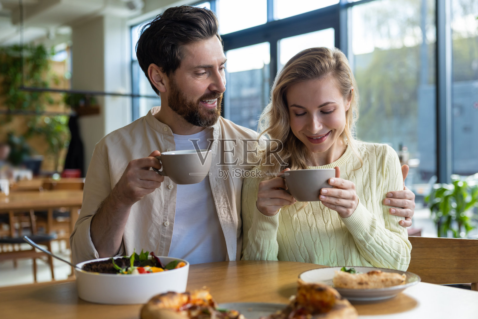 情侣在温馨的餐厅里分享咖啡和食物,桌上有沙拉和比萨饼。照片摄影图片