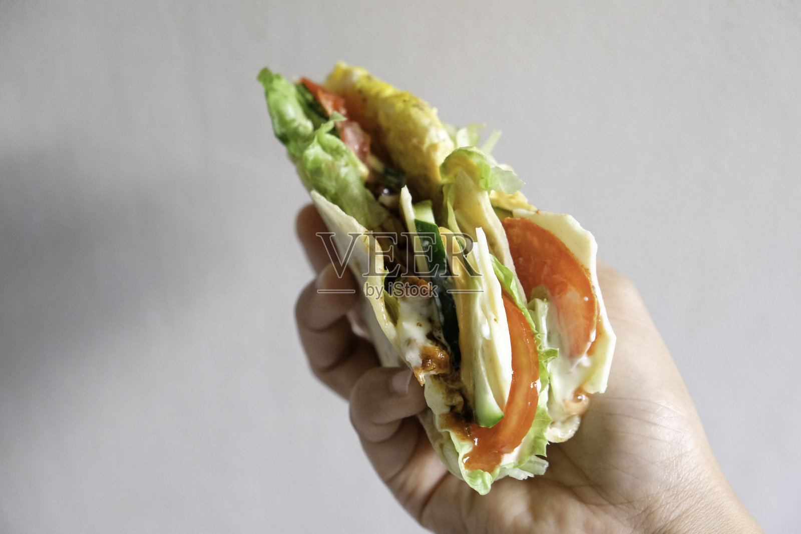 手握烤鸡肉和蔬菜的玉米饼卷照片摄影图片