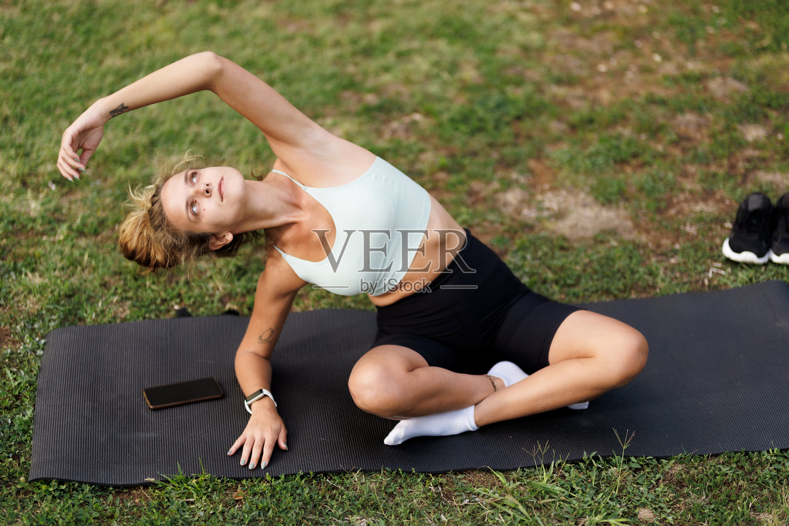 美丽的女性在阳光明媚的户外环境中,舒展身体,正在瑜伽垫上练习瑜伽。照片摄影图片