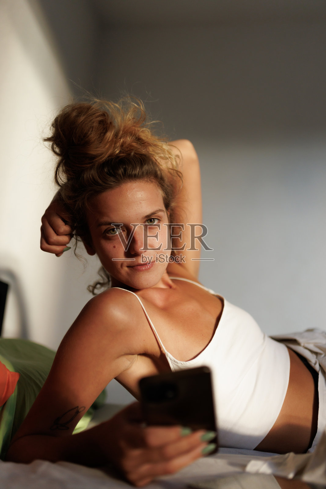 放松的女人在阳光明媚的下午卧室里躺在床上看手机照片摄影图片