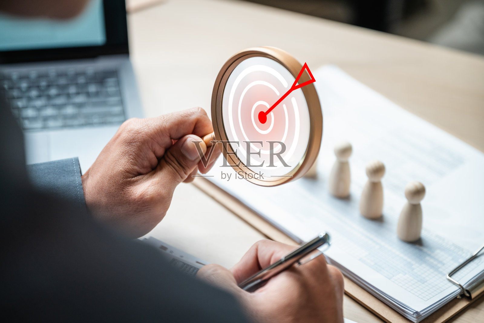 一个人用放大镜查看一张纸,上面有一个红色的靶子。照片摄影图片