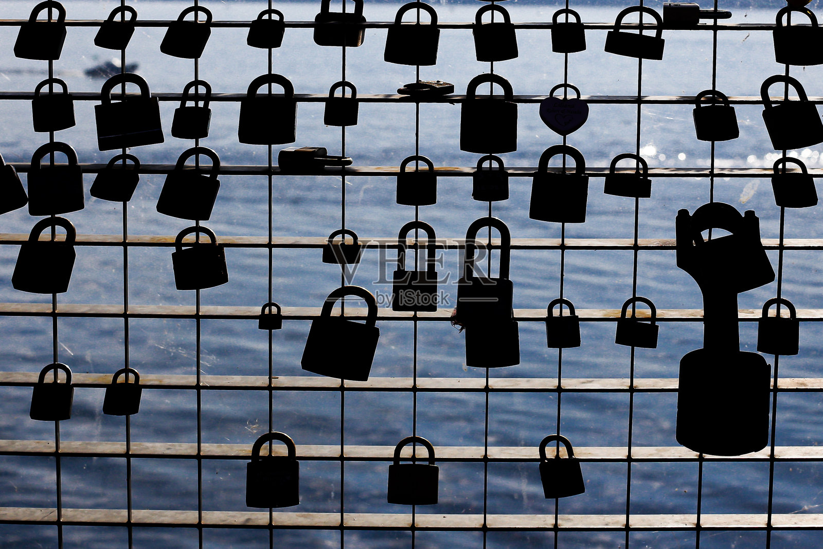 栅栏上的爱情锁。象征爱情的浪漫传统。金属挂锁与水面背景。照片摄影图片