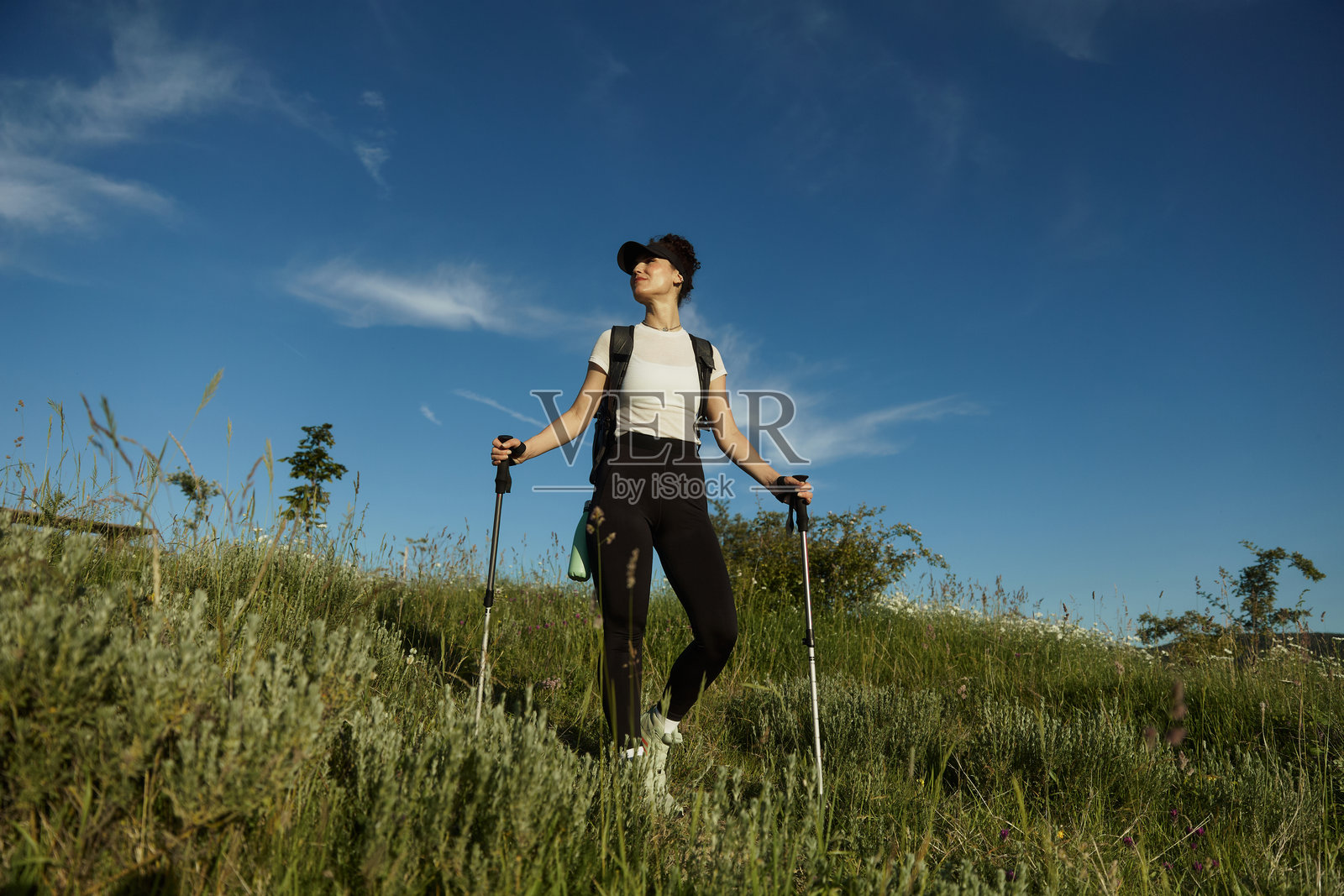 一位美丽的女性在高草田野中漫步,四周环绕着山丘。照片摄影图片
