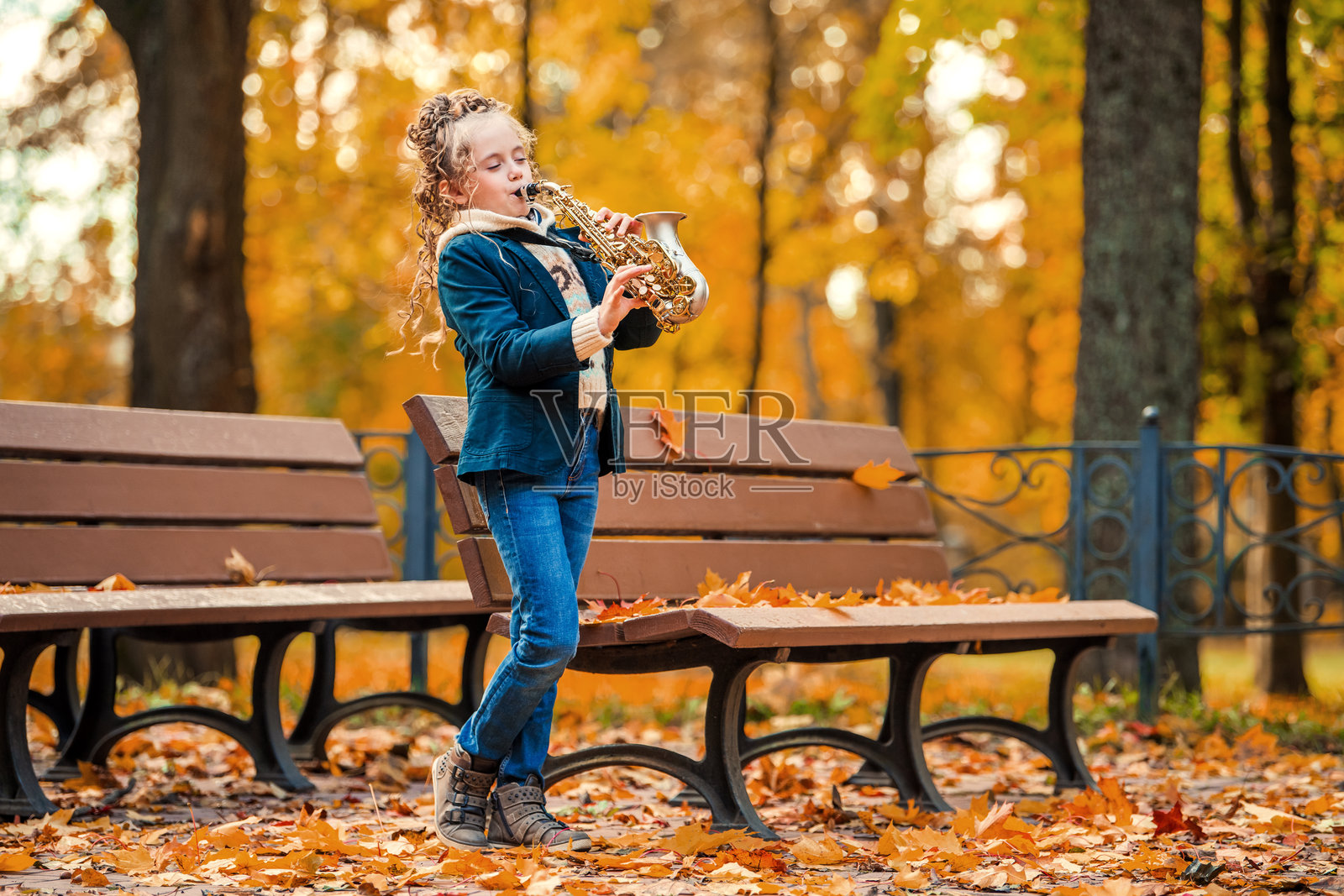 年轻女孩在秋天的公园里吹萨克斯风。照片摄影图片