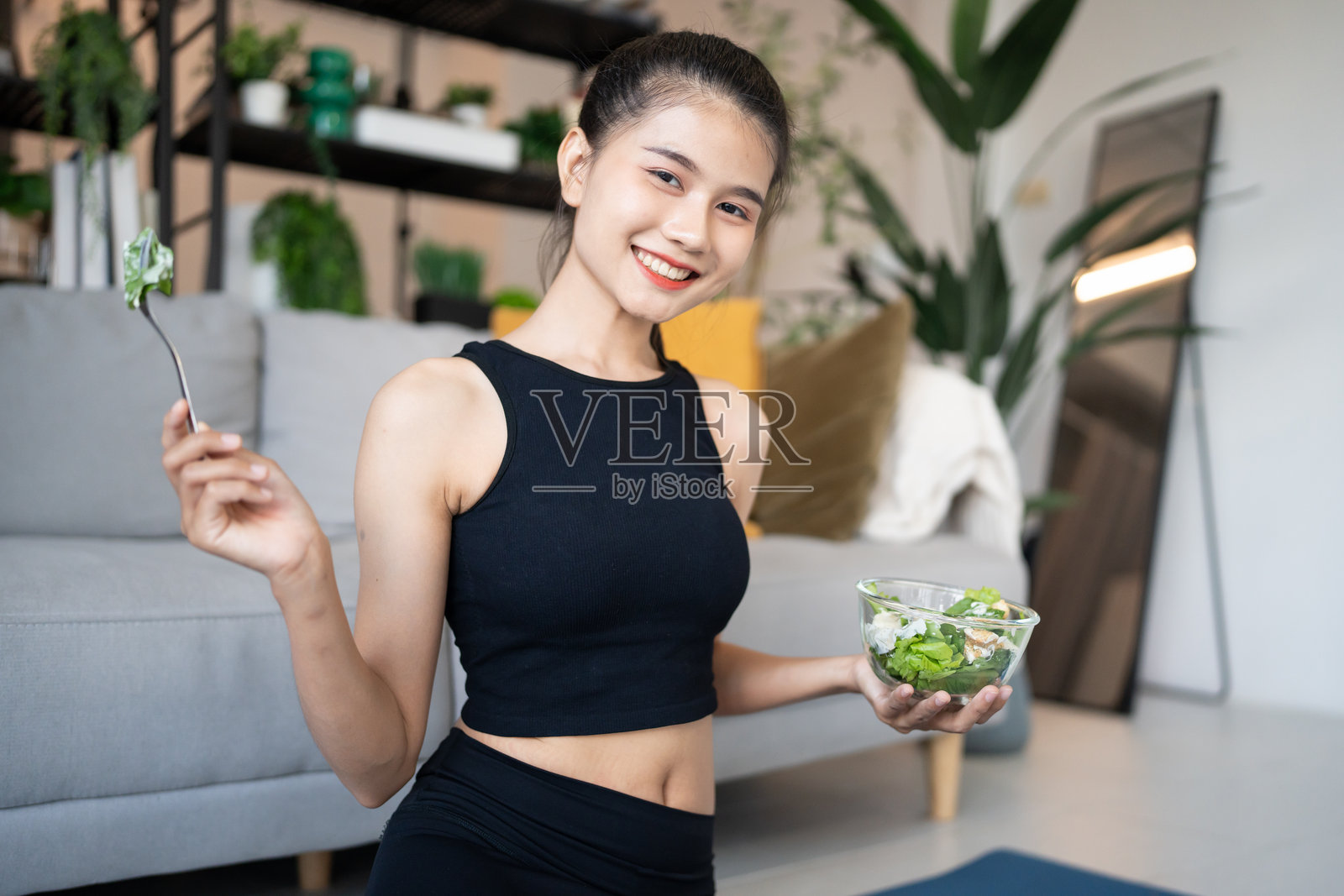 健身的亚洲女性在锻炼后享用健康沙拉,微笑着。美丽的亚洲年轻女性在瑜伽馆里吃健康食品,过着健康的生活方式。照片摄影图片