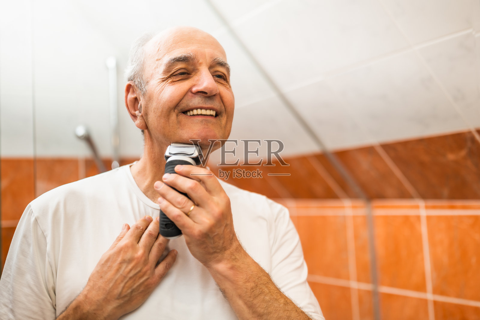 自信的老年男子在镜子前使用电动剃须刀修整仪容照片摄影图片