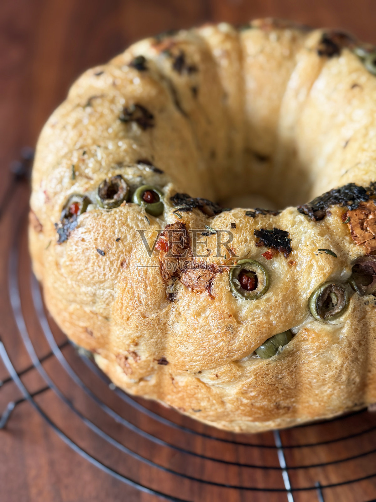 自制面包在环形蛋糕模具中烘焙,采用佛卡夏风格,配有橄榄和晒干番茄 / 酥脆的外壳放在冷却架上。照片摄影图片