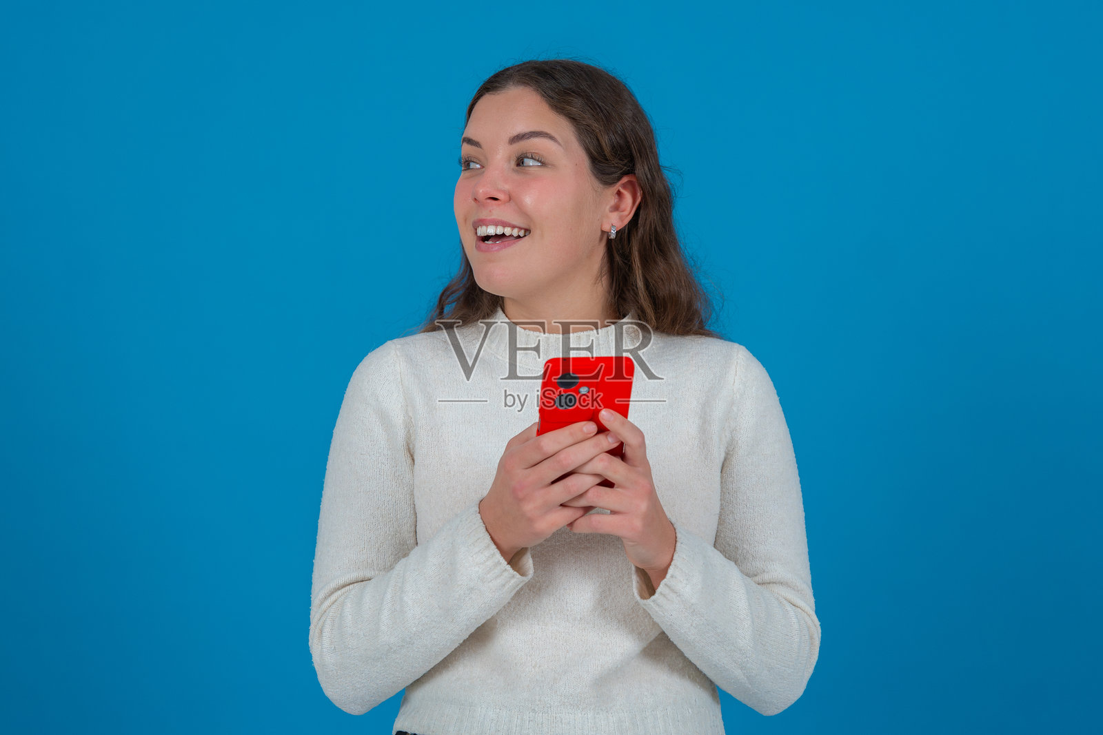 惊讶的年轻女性手持红色智能手机,背景为蓝色照片摄影图片