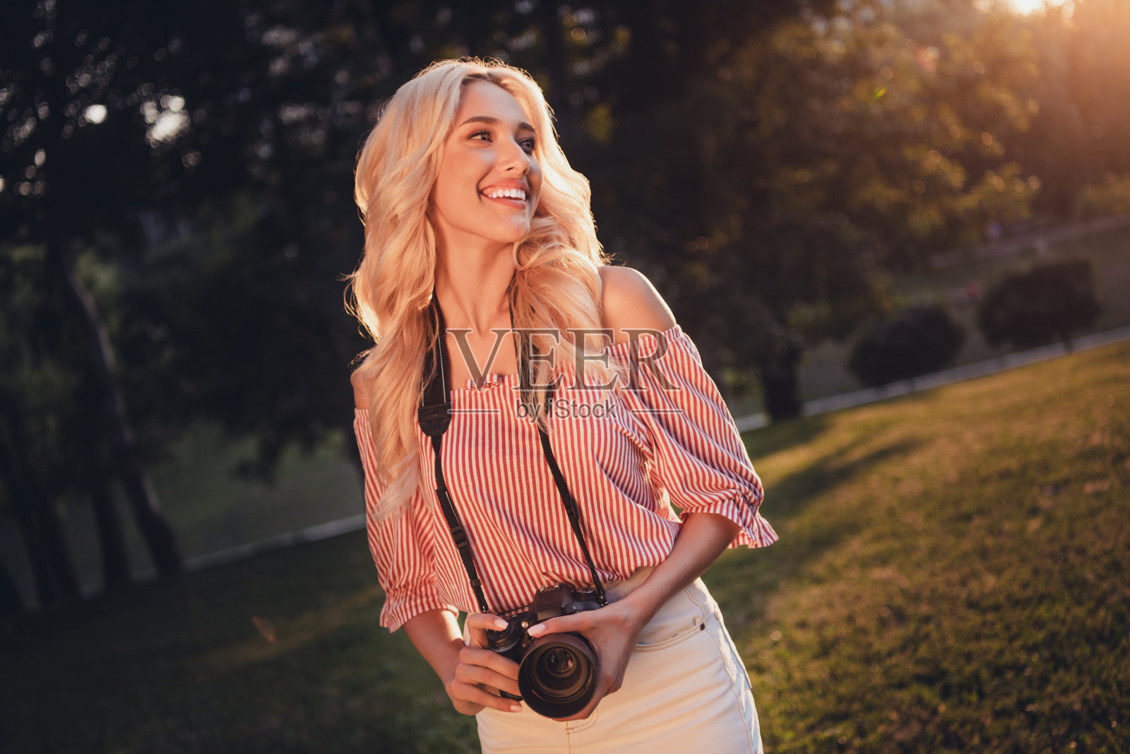 美丽满意的女士手持数码相机,目光投向远方,享受户外休闲时光。照片摄影图片