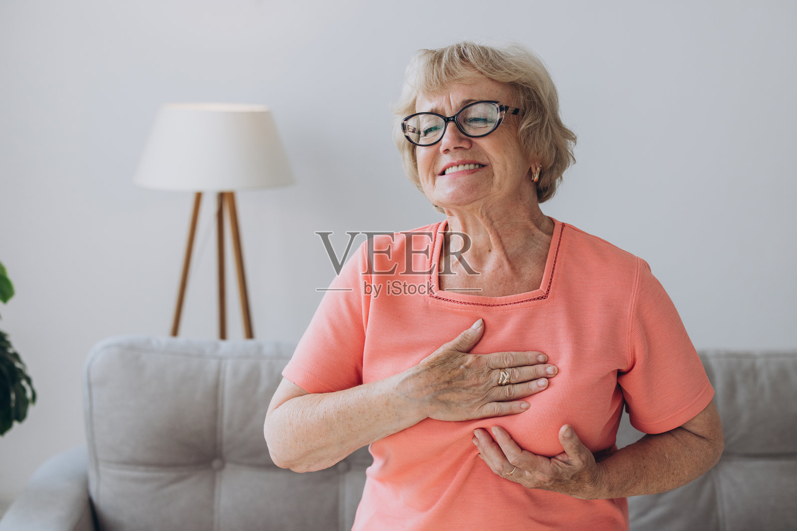 老年女性在客厅中感到心脏疼痛,按压胸部,经历心脏病发作,忍受着难以忍受的痛苦。照片摄影图片