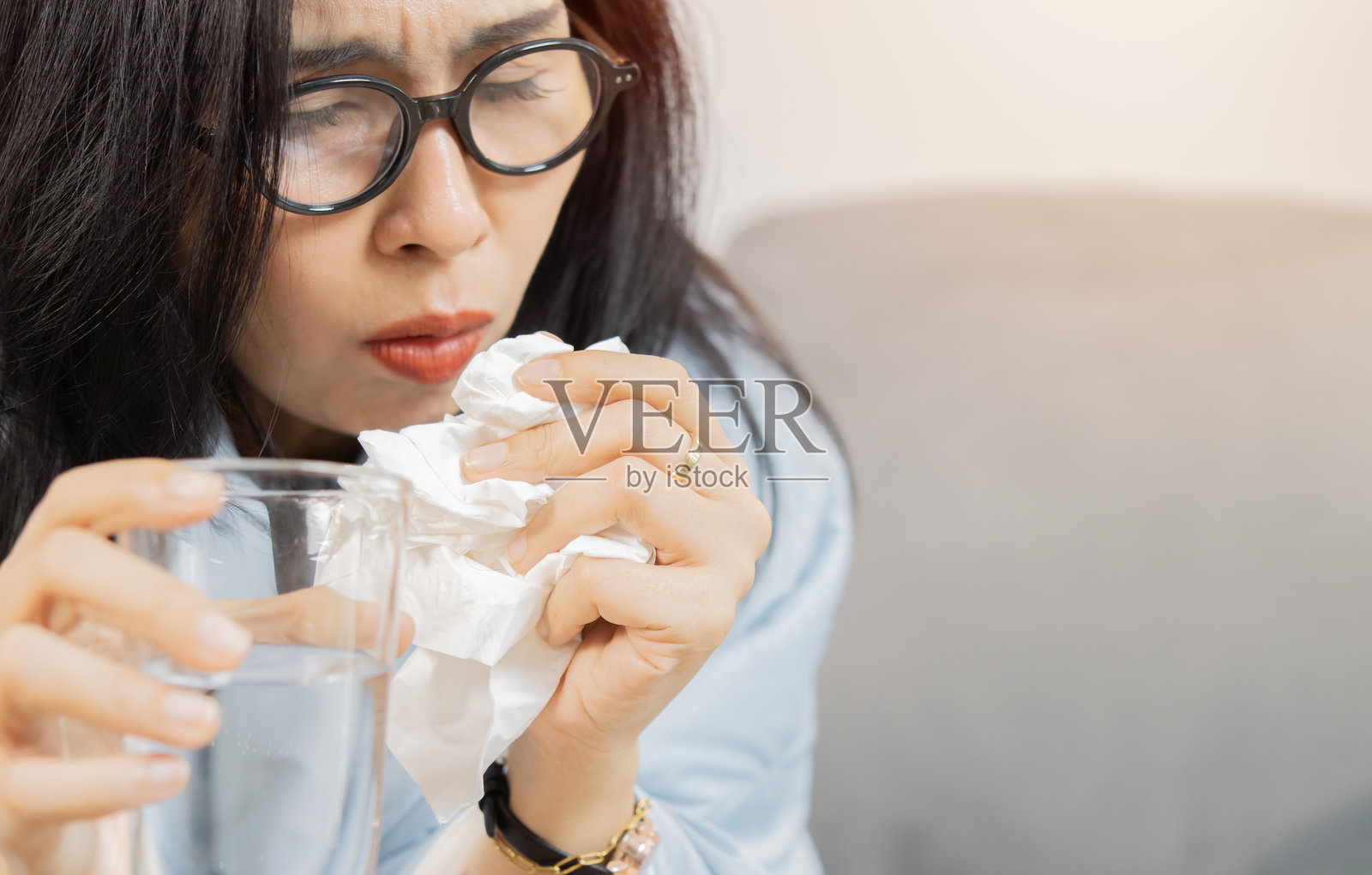 女性近距离特写,手持水杯和纸巾,因喉咙痛而咳嗽。照片摄影图片