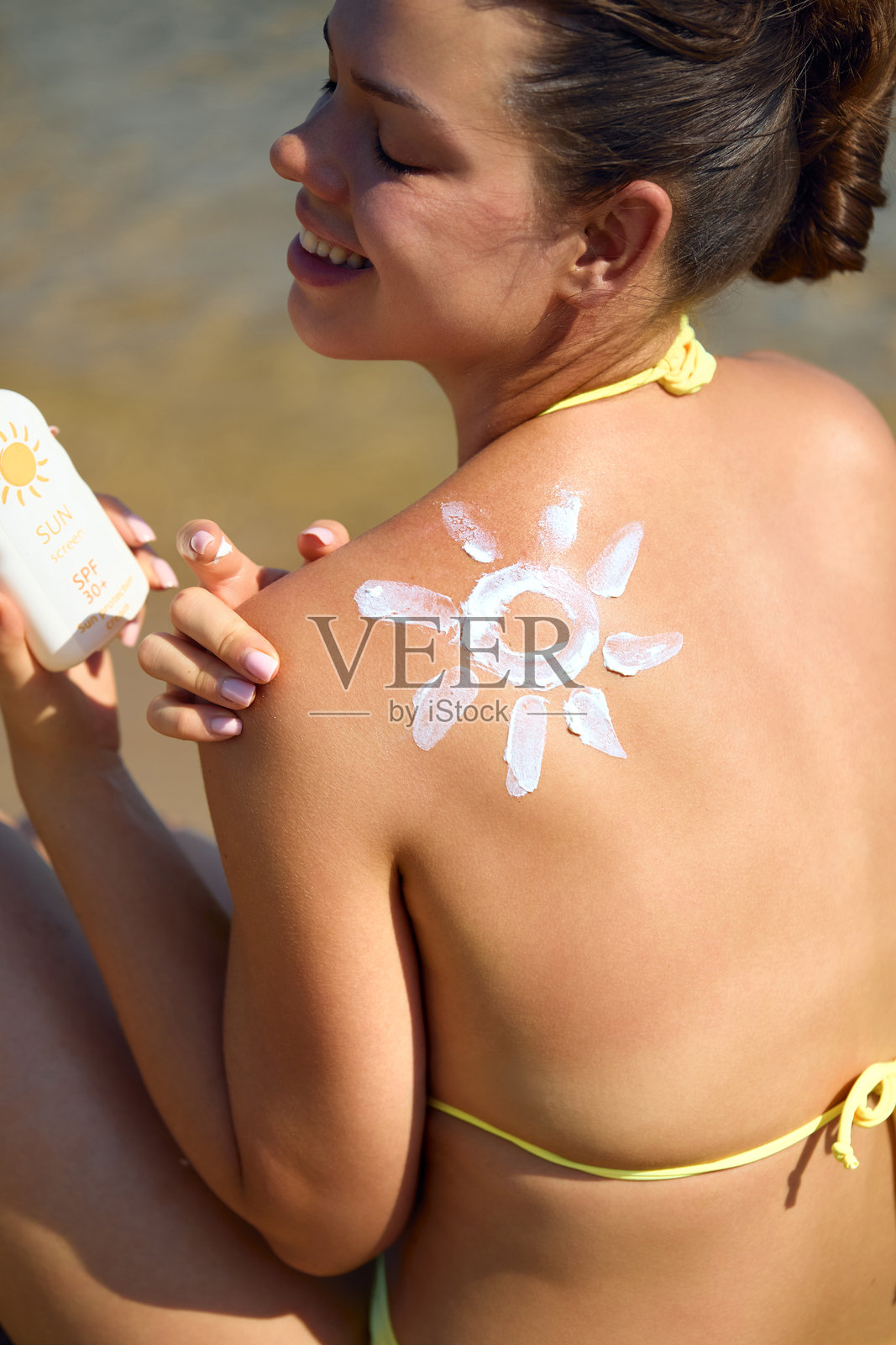 面部护理。年轻女性手持防晒霜瓶,微笑着涂抹在脸上。美丽的面容。年轻女性戴着帽子,涂抹保湿乳液在肌肤上。护肤。照片摄影图片