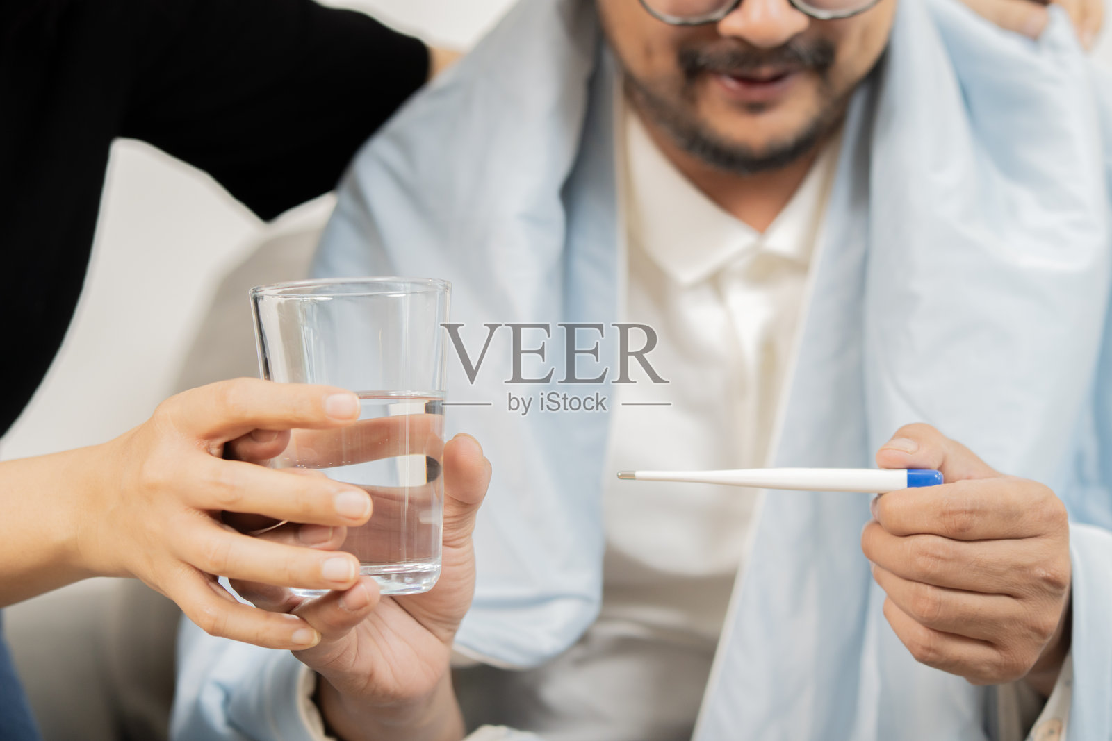 成熟夫妇在家中查看温度计测量体温,并手持一杯水。照片摄影图片