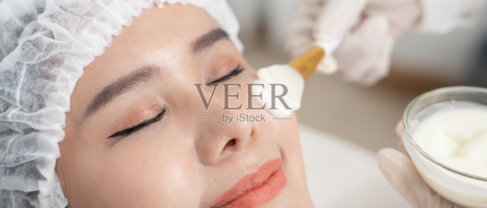 美丽的女性正在接受面部水疗和护理。健康女性的面部涂抹面霜。皮肤霜的广告,抗皱、婴儿般的面容、美白、保湿、收缩毛孔精华。照片摄影图片