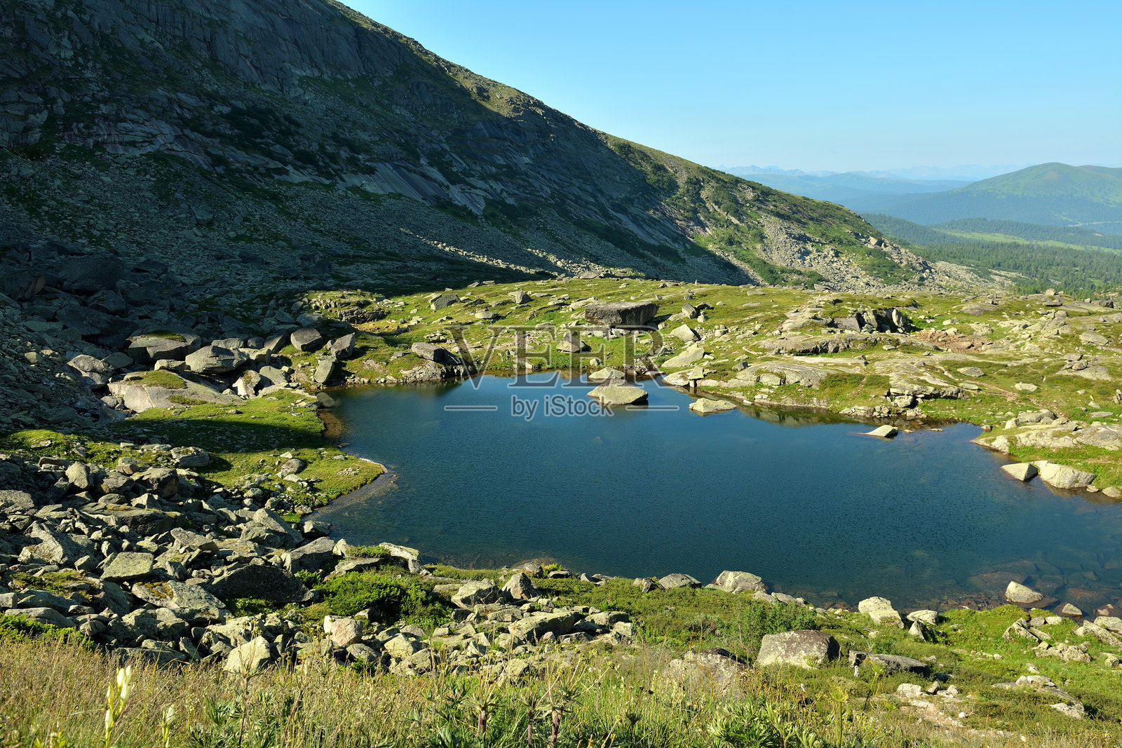 一个风景如画的小湖,湖边散落着岩石,位于高悬崖的脚下,阳光明媚的夏日早晨。照片摄影图片