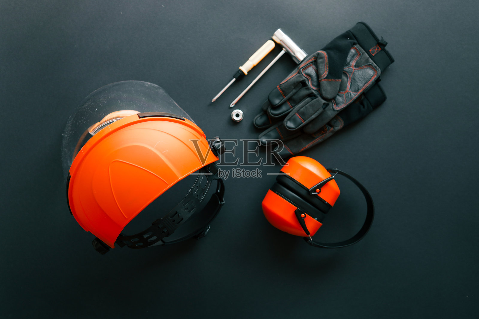 安全面罩、耳罩、工作手套、螺丝刀、扳手和螺母排列在深色背景上。用于维护园艺割灌机的防护设备和工具套件。照片摄影图片