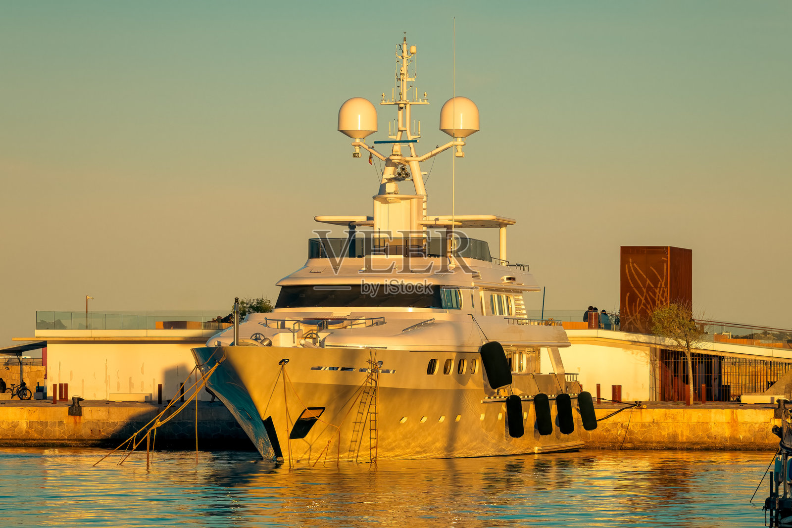 一艘白色豪华游艇停靠在西班牙伊比萨岛的码头,背景是晴朗的日落天空。照片摄影图片