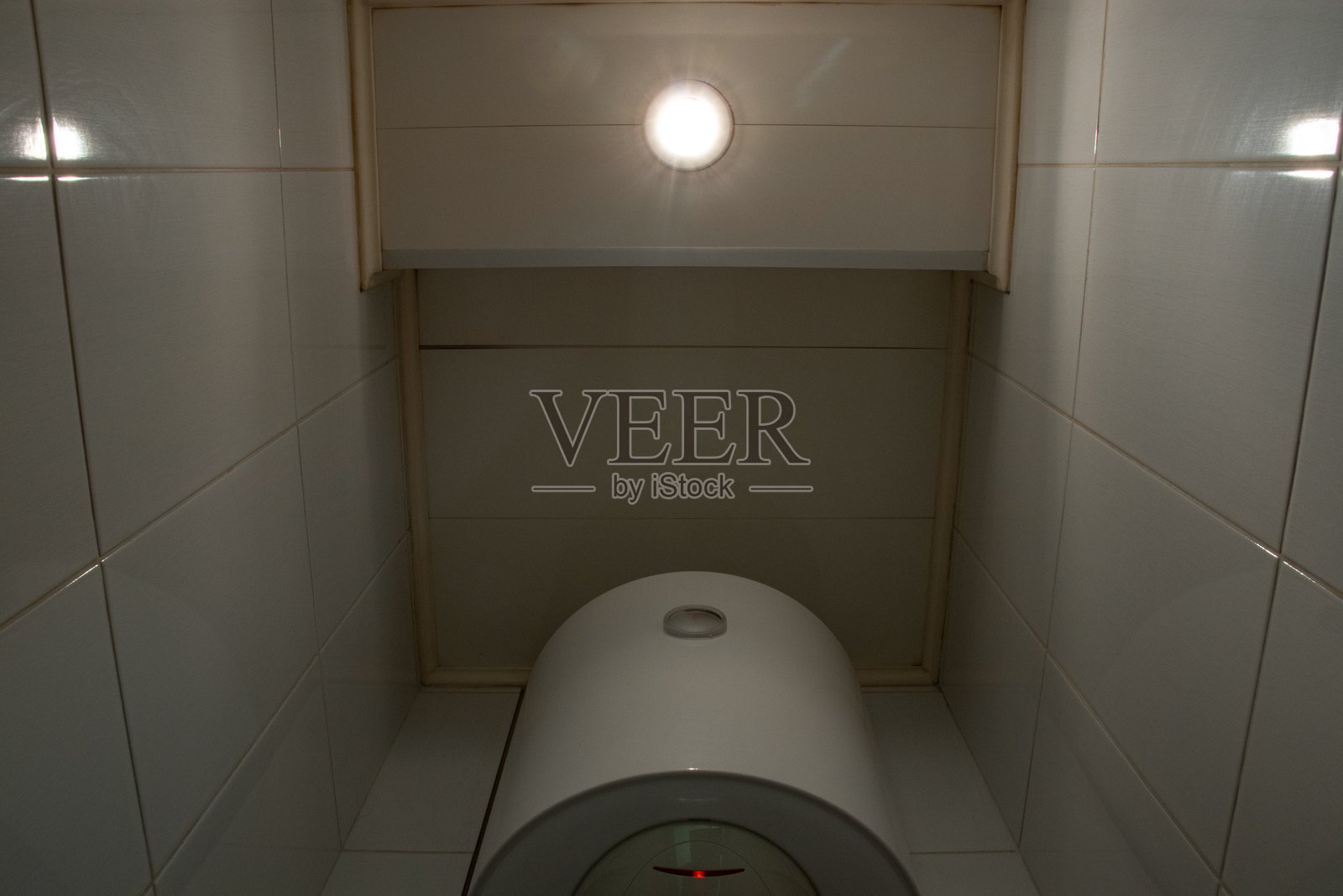 从底部向上看厕所里的热水器,瓷砖墙壁和天花板灯,空间小,厕所。照片摄影图片