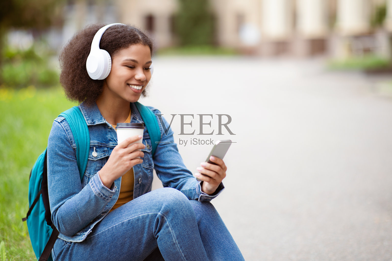 学生休闲。年轻的黑人女性在户外使用智能手机并喝咖啡。照片摄影图片