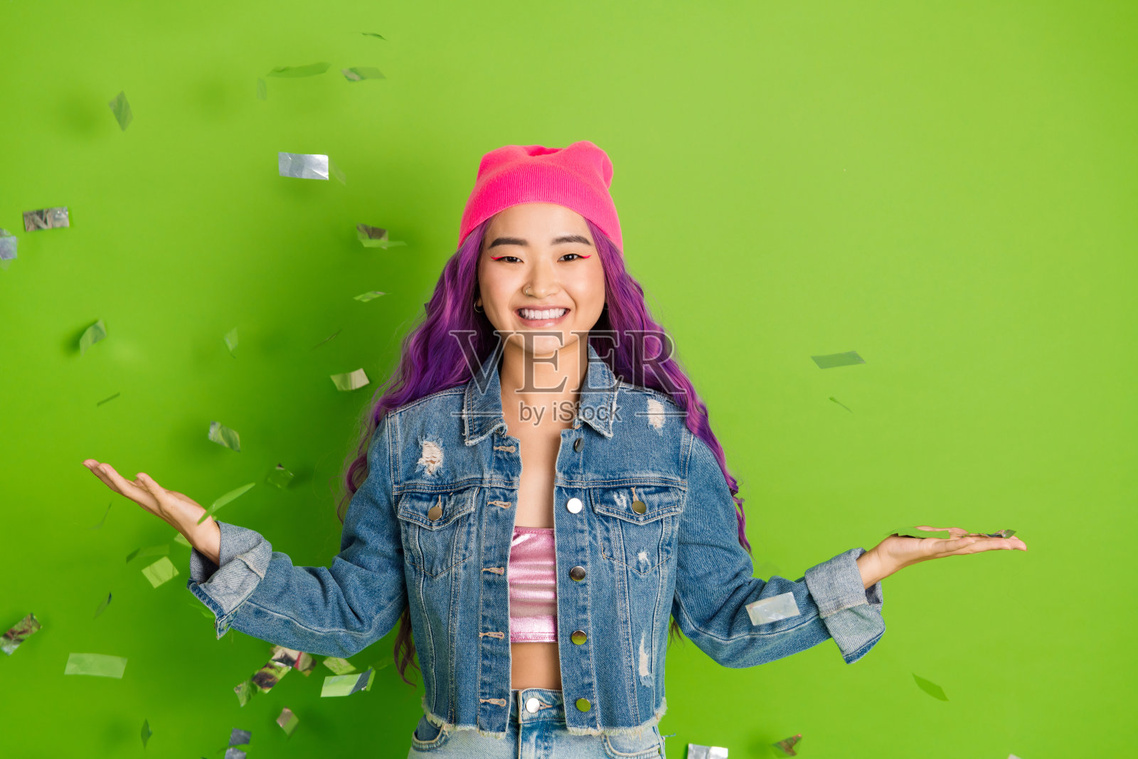 一位年轻的女性,染着紫色头发,穿着休闲风格,在鲜艳的绿色背景上欢快地庆祝。照片摄影图片