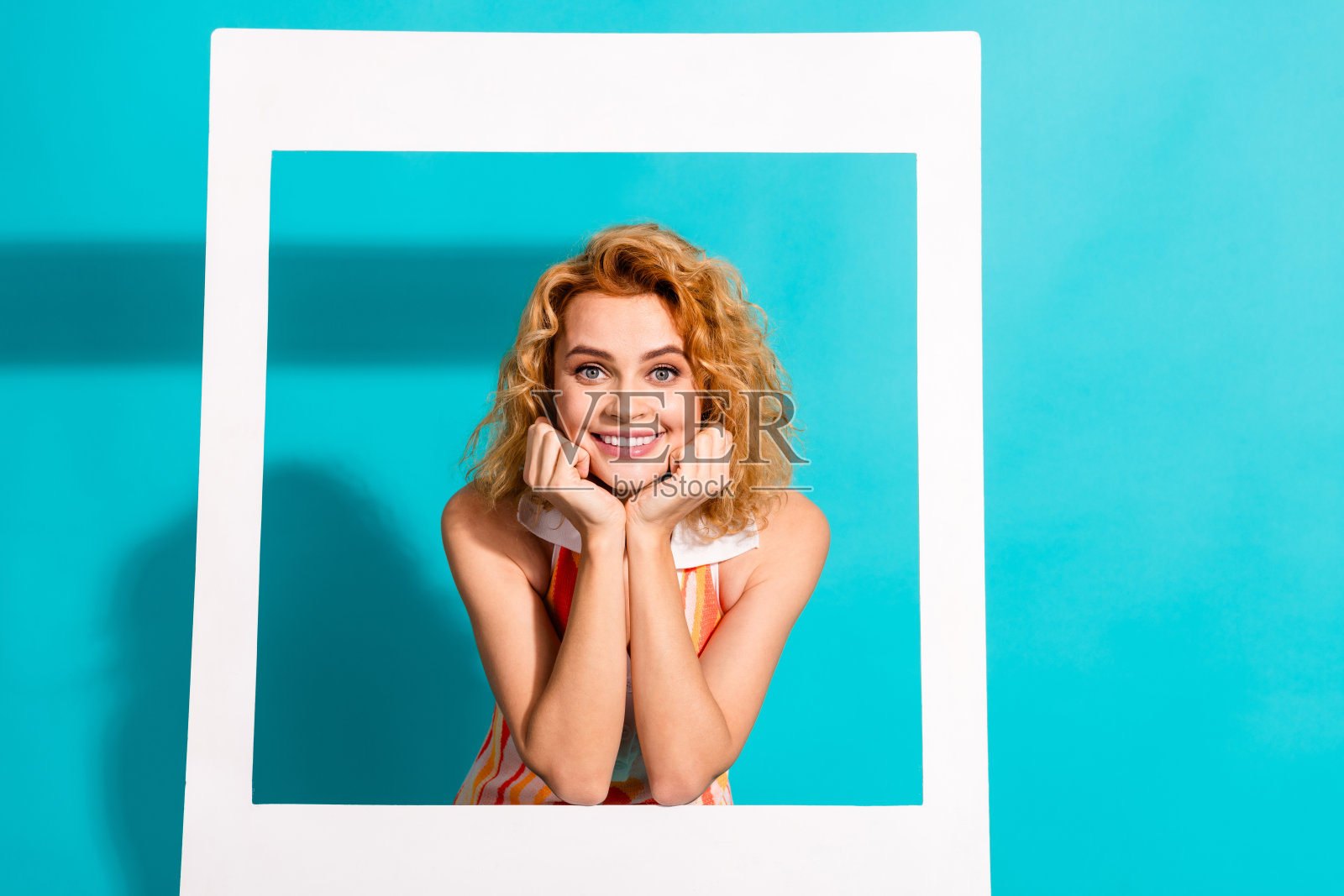 微笑的年轻女性,红色卷发,穿着休闲迷人的服装,背景为青绿色,白色边框装饰。照片摄影图片