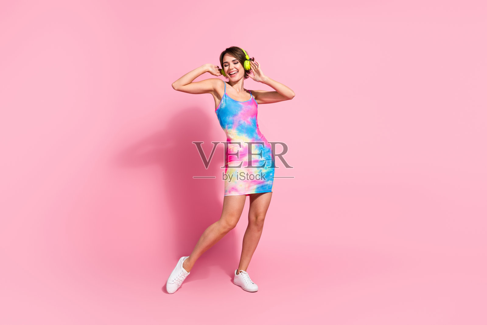 年轻女性穿着色彩斑斓的夏季连衣裙,站在粉色背景前,散发出快乐和自信。照片摄影图片