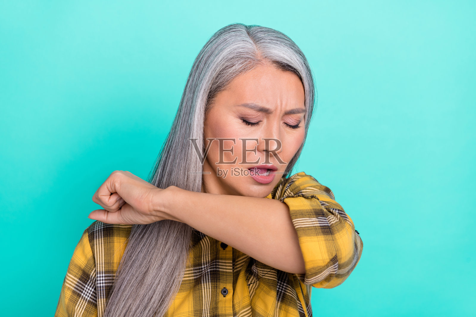 成熟的亚洲女性因新冠病毒症状而感到不适,独自一人,背景为青绿色。照片摄影图片