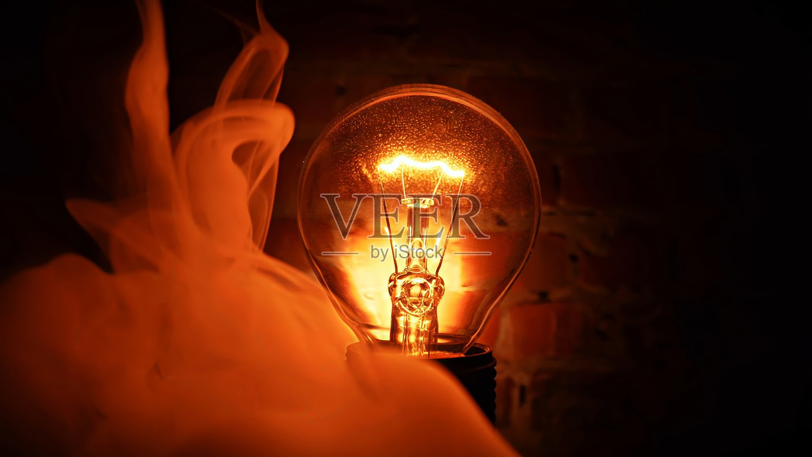 黑色背景下的钨丝灯泡,伴随着袅袅烟雾。照片摄影图片