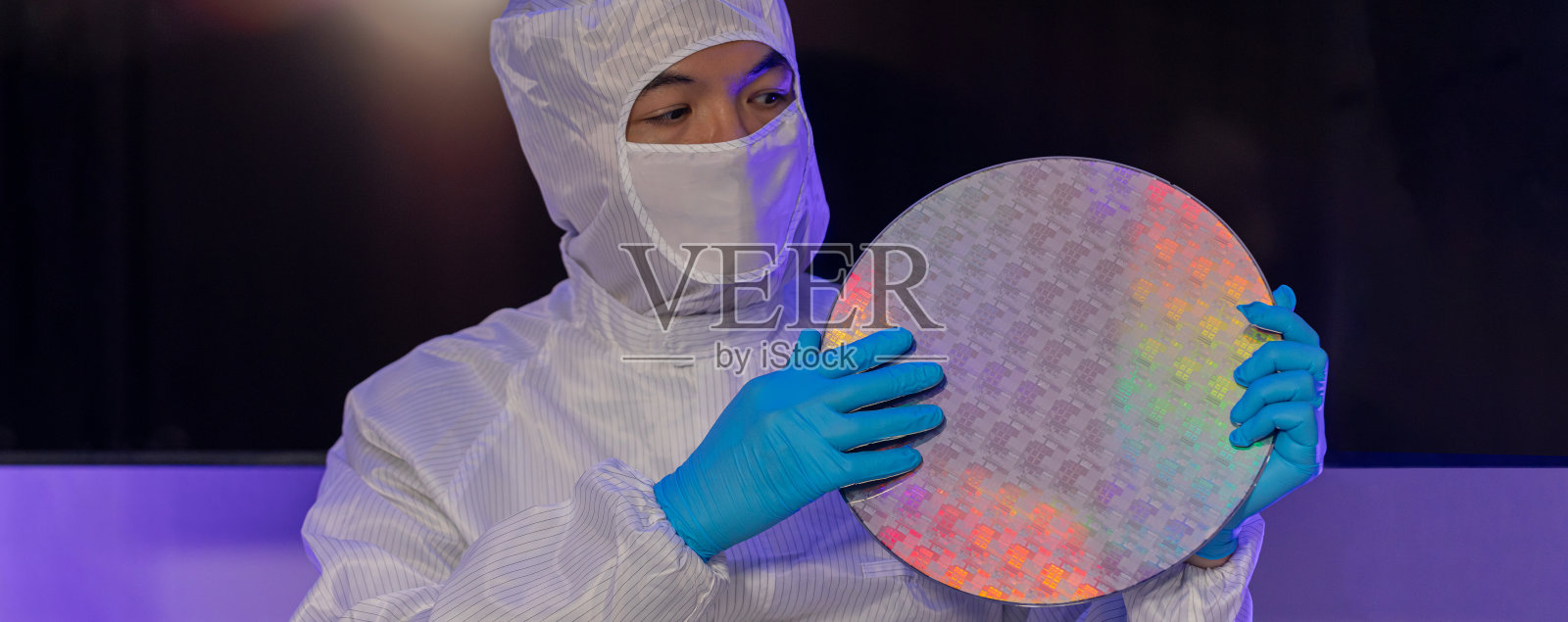 电子制造厂的半导体生产。工人或工程师穿着医疗防护服或白色工作服,手持硅晶圆。照片摄影图片