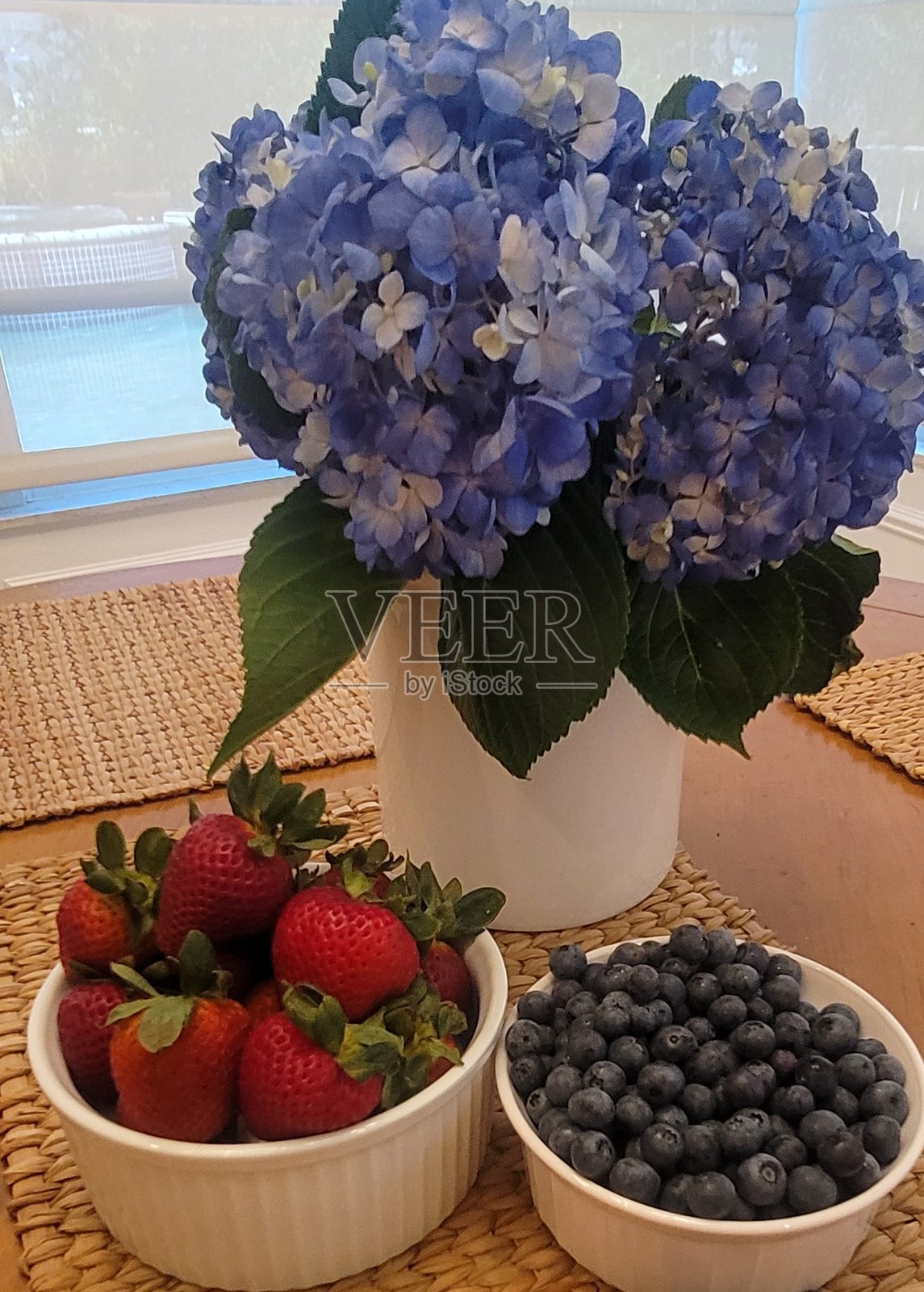 装有蓝色绣球花的花瓶,旁边是准备食用的草莓和蓝莓碗。照片摄影图片