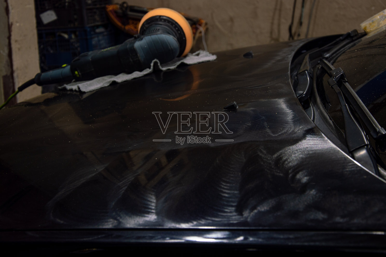 一辆黑色汽车的引擎盖正在用机器打磨,展示了在昏暗的车库环境中精细的工作。照片摄影图片