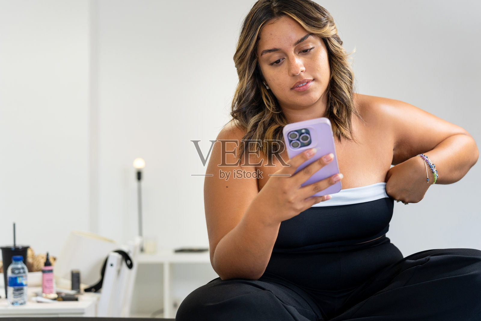 拉丁裔女性在眉毛拉伸治疗后查看手机。照片摄影图片